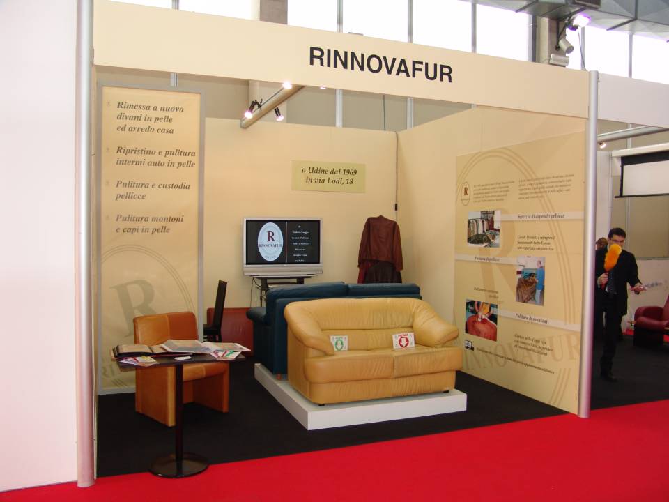 Stand espositivo con divano beige, schermo TV e pannelli a parete con la scritta 