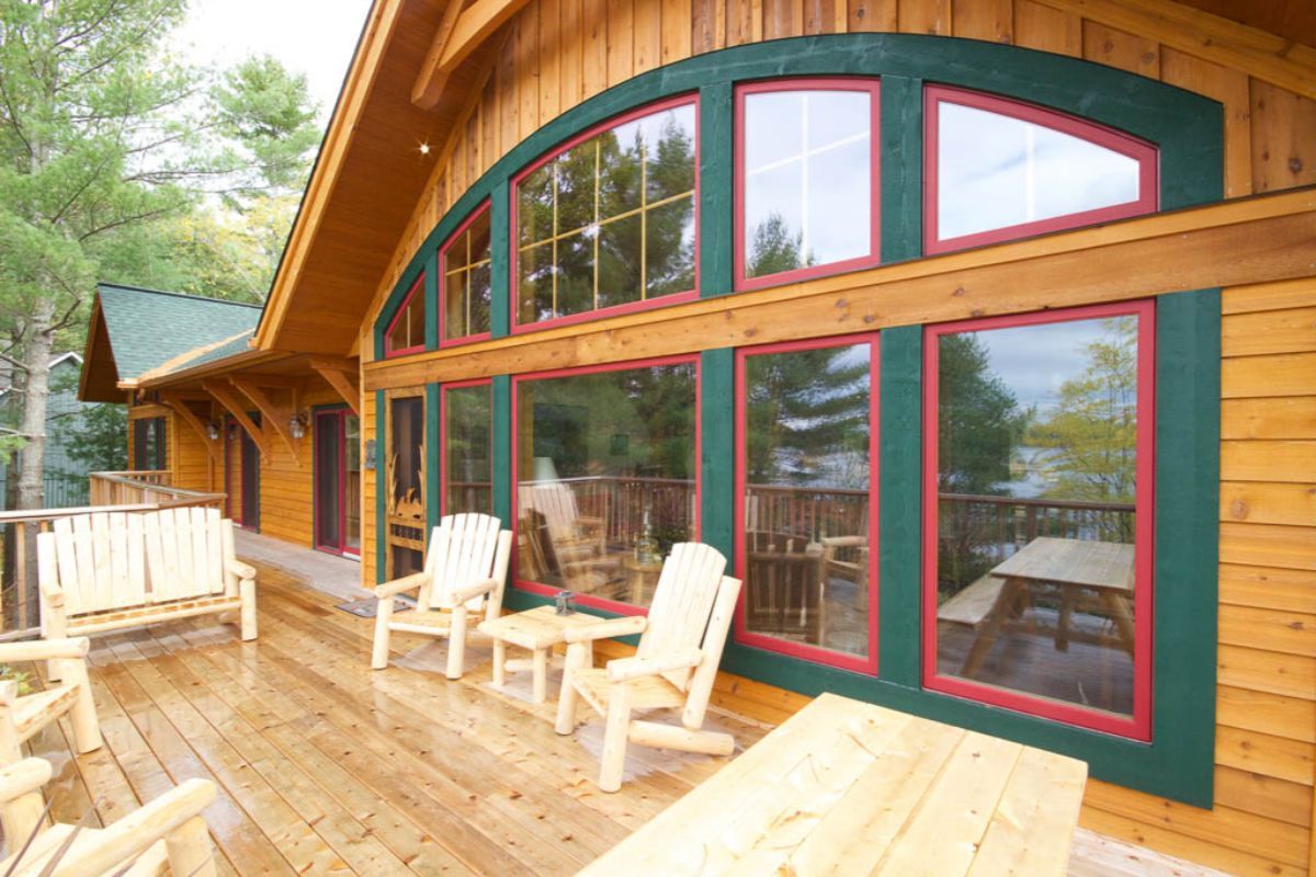 Custom Muskoka Cottage featuring a large wooden house with lots of windows and chairs on the deck