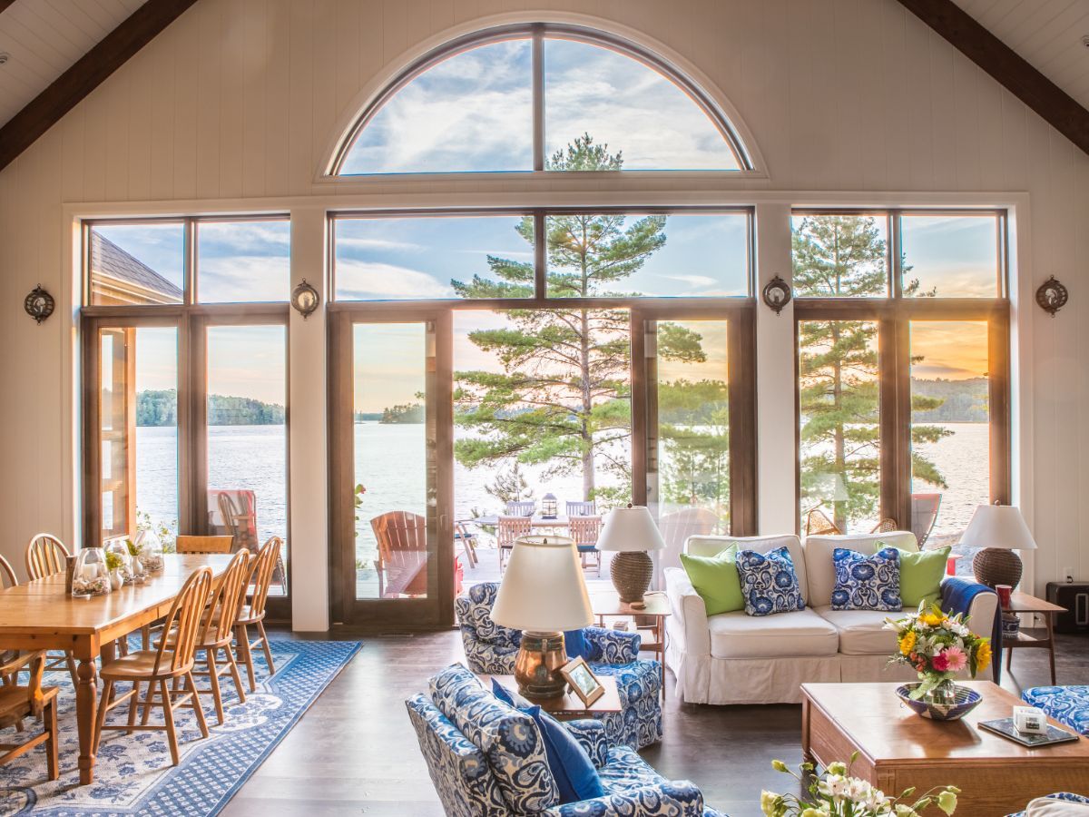 Custom Muskoka Cottage featuring a living room with a couch , chairs and a table with a view of a lake.