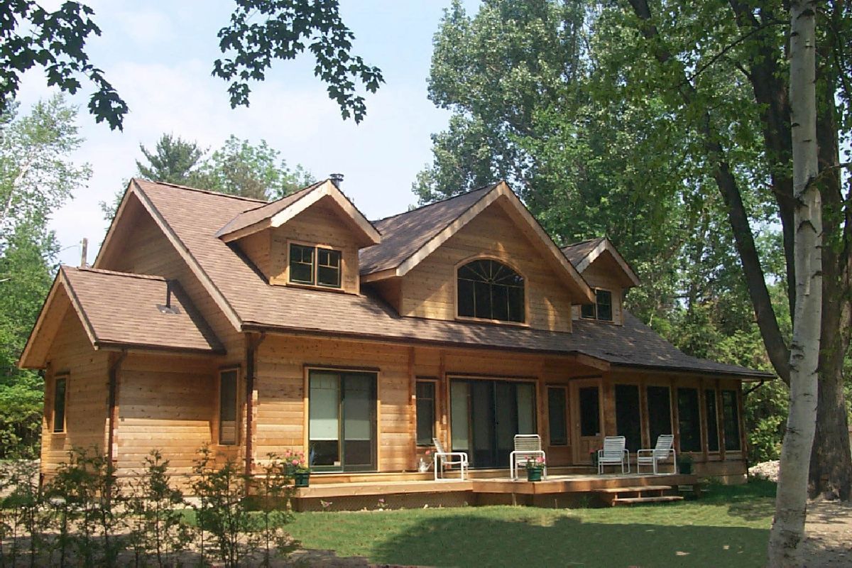 Custom Muskoka Cottage featuring a large wooden house with a brown roof is surrounded by trees