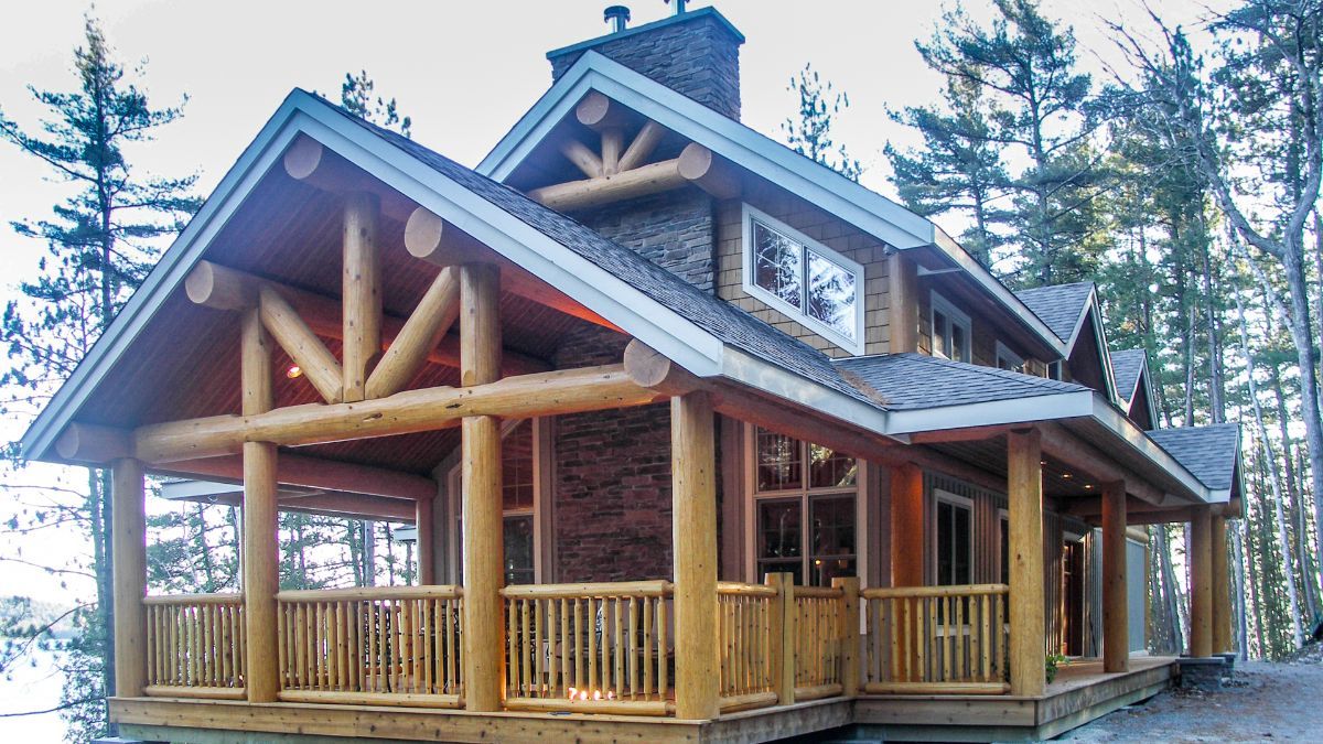 Custom Muskoka Cottage featuring a large log cabin with a large porch in the woods