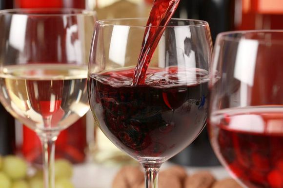 Un bicchiere di vino rosso viene versato in un altro bicchiere, tra diversi altri calici da vino.