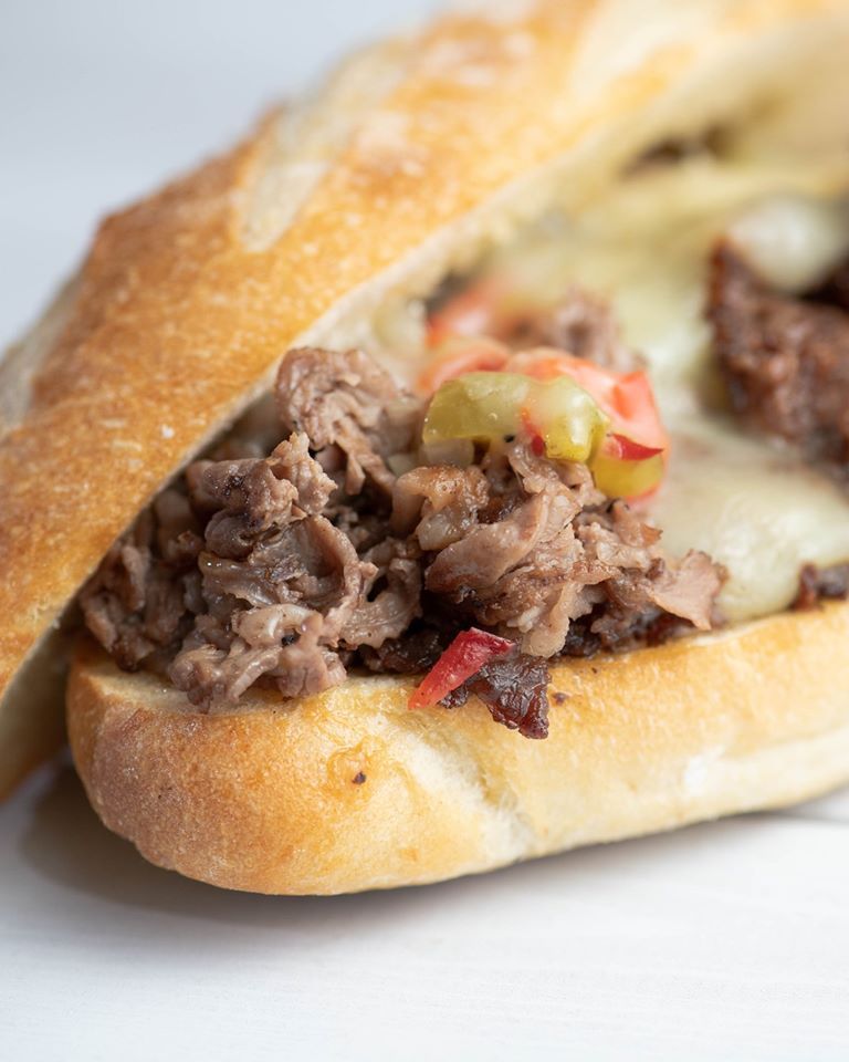 A close up of a steak sandwich on a bun on a table.