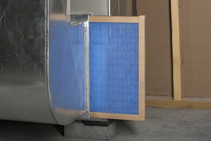 Electrician Opening Lid Of AC — Kalamazoo, MI — Suburban Heating & Air Conditioning Air filter in a metal duct. The blue filter is in a cardboard frame, set in a gray concrete setting.