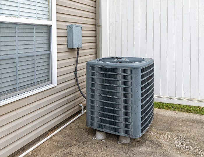 AC Service and Maintenance — Kalamazoo, MI — Suburban Heating & Air Conditioning Outdoor air conditioning unit next to a house with beige siding and a window.