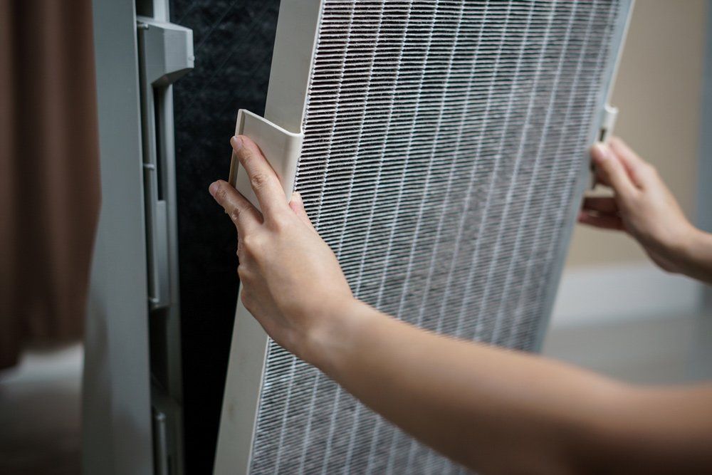 Air Filtration — Kalamazoo, MI — Suburban Heating & Air Conditioning Hands replacing an air purifier filter.