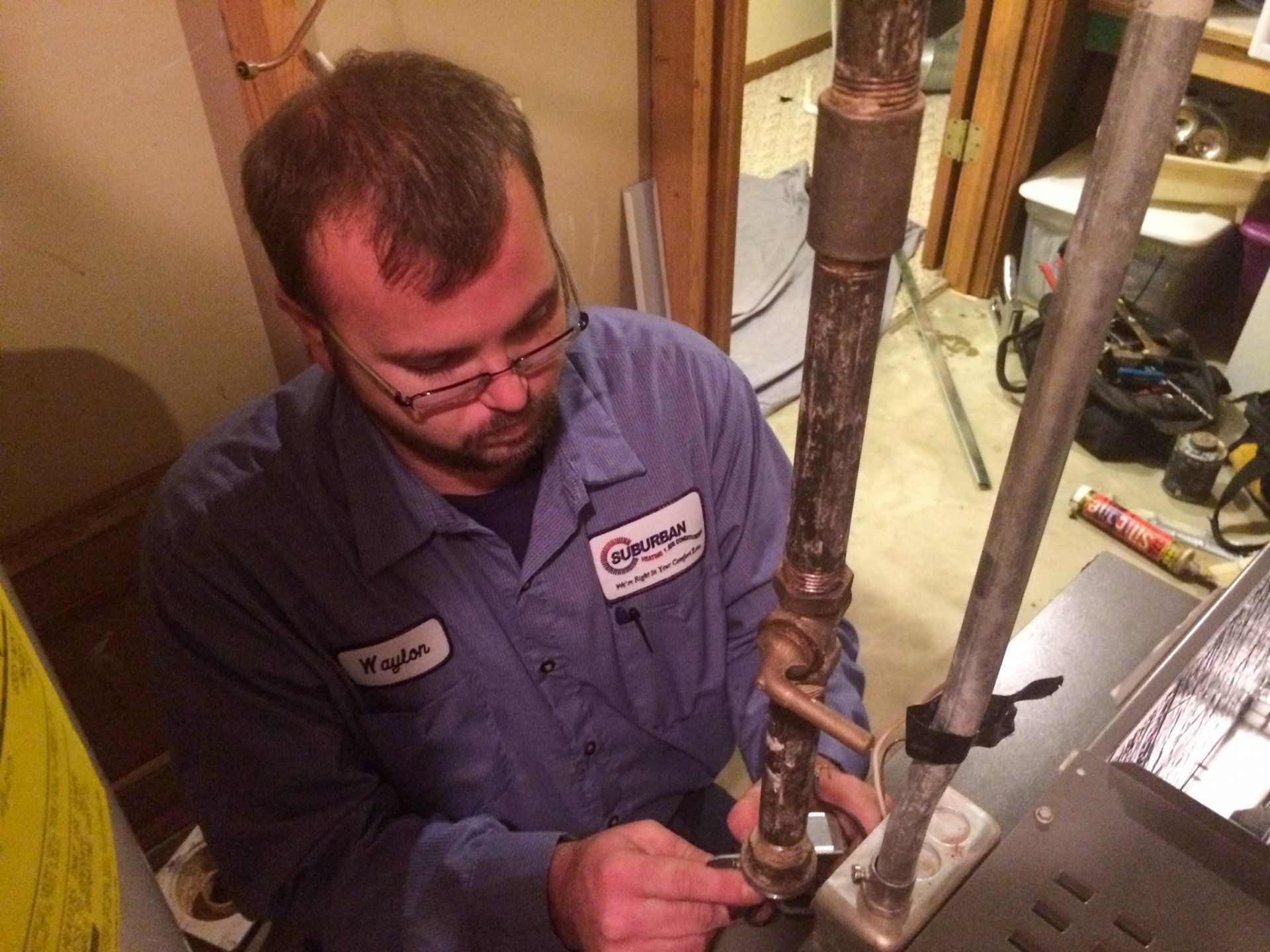 AC Installation — Kalamazoo, MI — Suburban Heating & Air Conditioning Plumber in blue uniform working on a pipe in a basement.