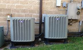 Two outdoor air conditioning units next to a brick wall.