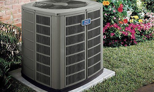 Outdoor air conditioning unit with garden background. Gray unit, brick wall, and flowers.
