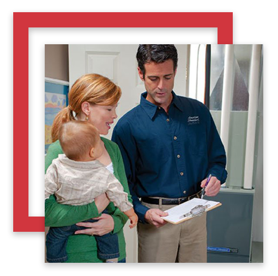 Man in blue shirt reviews a clipboard with a woman holding a baby in a home setting.