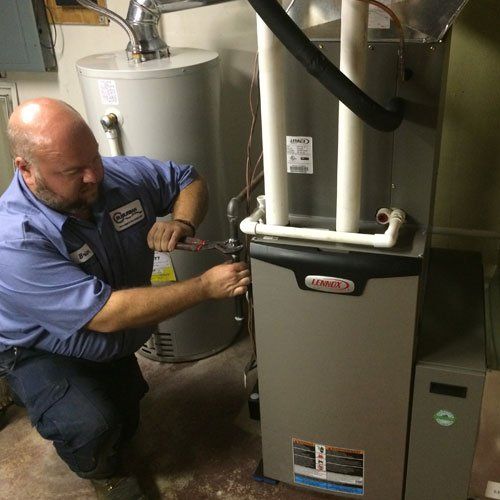 Technician in blue uniform working on furnace and water heater in a utility room.
