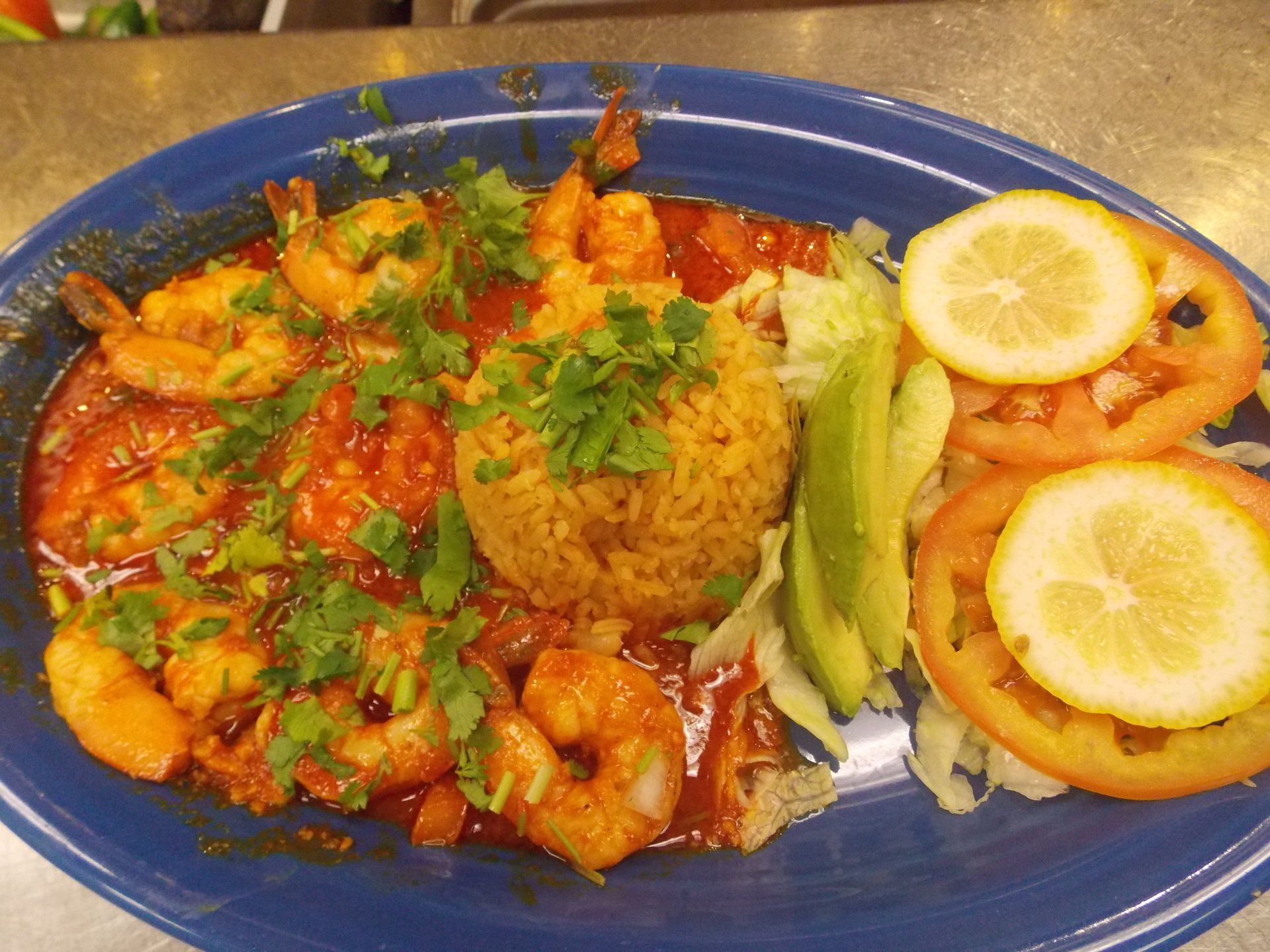 A blue plate topped with shrimp , rice , tomatoes and lemon slices.