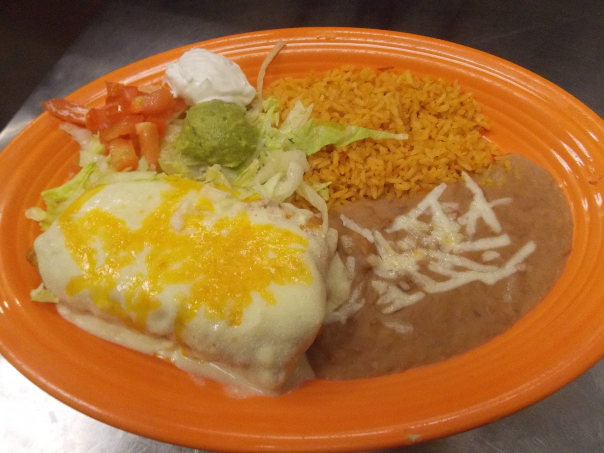An orange plate topped with a burrito , rice and beans.
