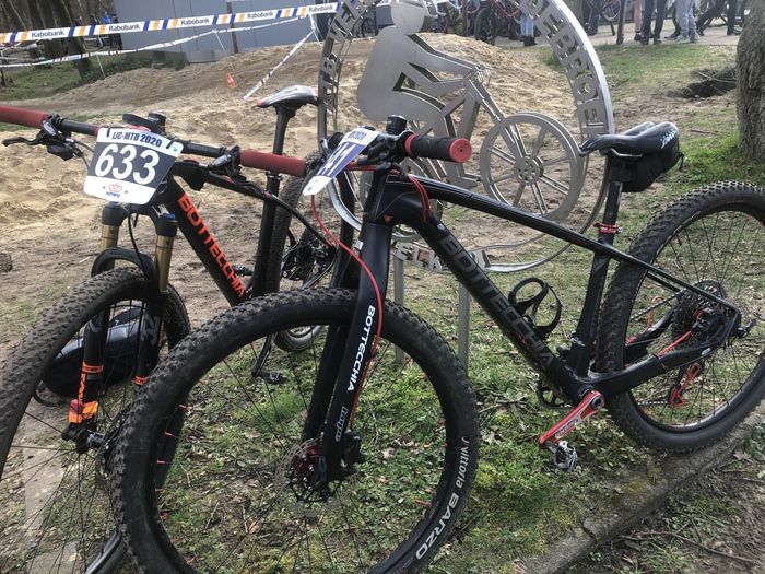 Twee mountainbikes met startnummers op een grasveld, waarvan één zwart met rode accenten.