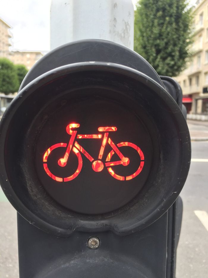 Rood fietsverkeerslicht verlicht op een zwarte achtergrond, tegen een straatbeeld.