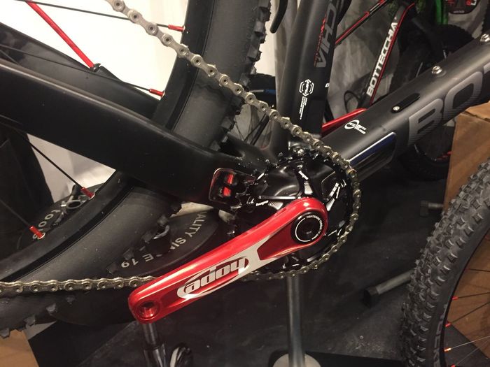 Detailopname van een zwarte fietsaandrijving met een rode crankarm en kettingblad.