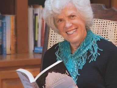 A picture of author janet howle sitting in a chair holding her novel uncharted and smiling.
