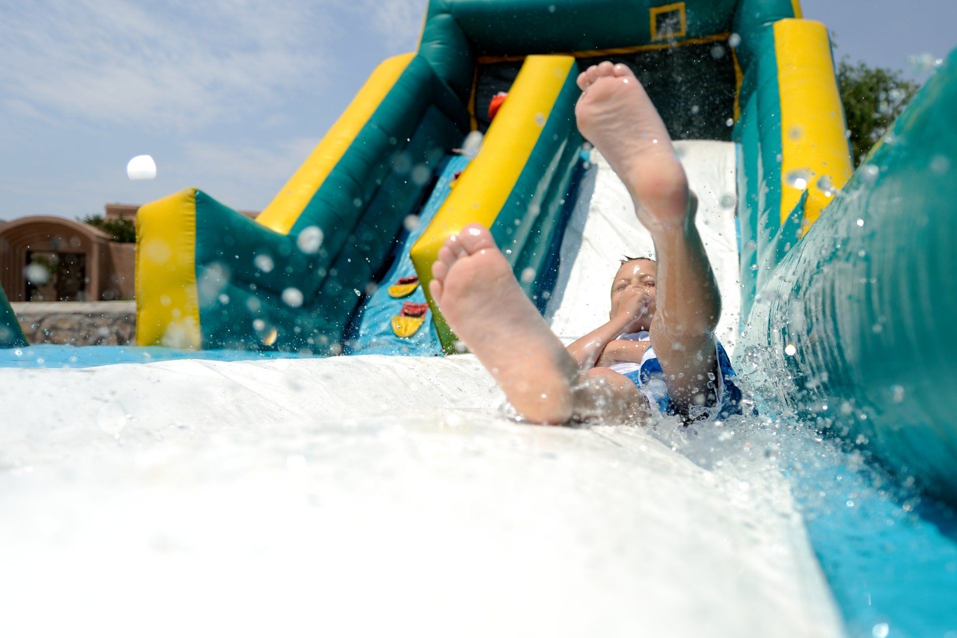 Splash! Young boy sliding down an inflatable water slide feet first while splashing water