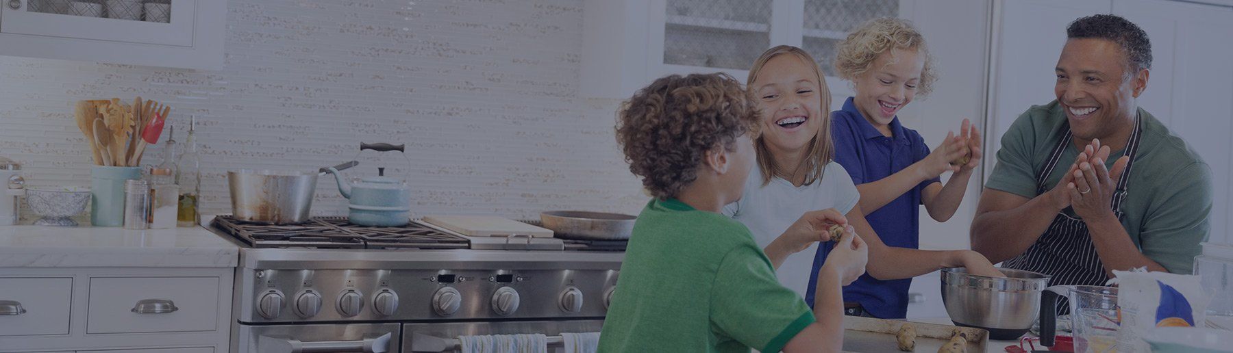 Family cooking in a kitchen, children laughing, father clapping near stove.