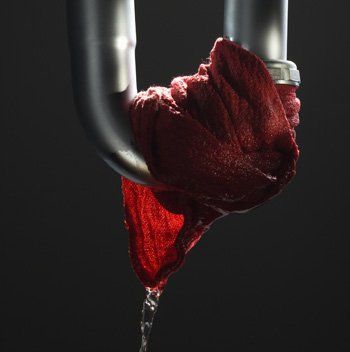 leaky pipe Red cloth stuffed in a silver pipe, water dripping from the cloth against a dark background.