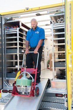 sewer line cleaning Man pushing a red and silver drain cleaning machine down a ramp from a yellow service truck.