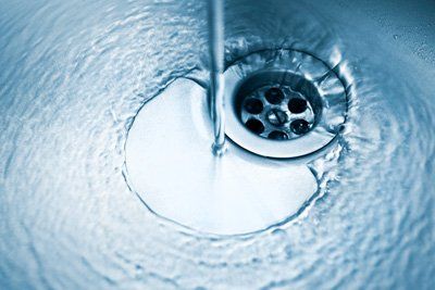 Water flowing into a drain in a stainless steel sink.