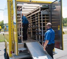 firm upfront pricing Two men loading shelves in a yellow delivery truck. One is inside, the other on the ramp.