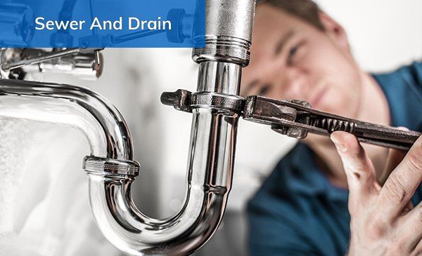 Plumber using a wrench to repair a silver pipe beneath a sink.