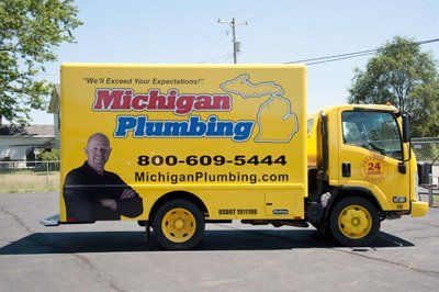 licensed backflow Yellow Michigan Plumbing truck with logo and phone number parked outdoors.