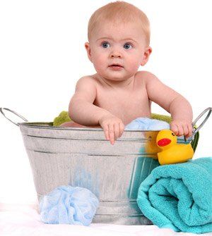 Baby sitting in a metal tub, surrounded by towels and a rubber duck.
