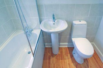 Bathroom with white fixtures: bathtub, pedestal sink, and toilet, on wood-look flooring.