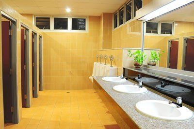 outstanding service Public restroom with multiple stalls, sinks, and mirrors; tan tile walls and floor.