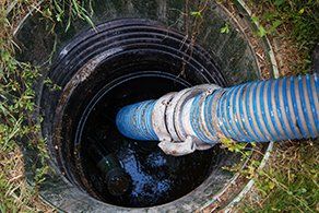 Drain Cleaning Service — Holt, MI — Michigan Plumbing Blue hose inserted into a dark septic tank, surrounded by grass.