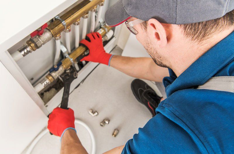 Plumber in blue shirt and red gloves uses a wrench on copper pipes.