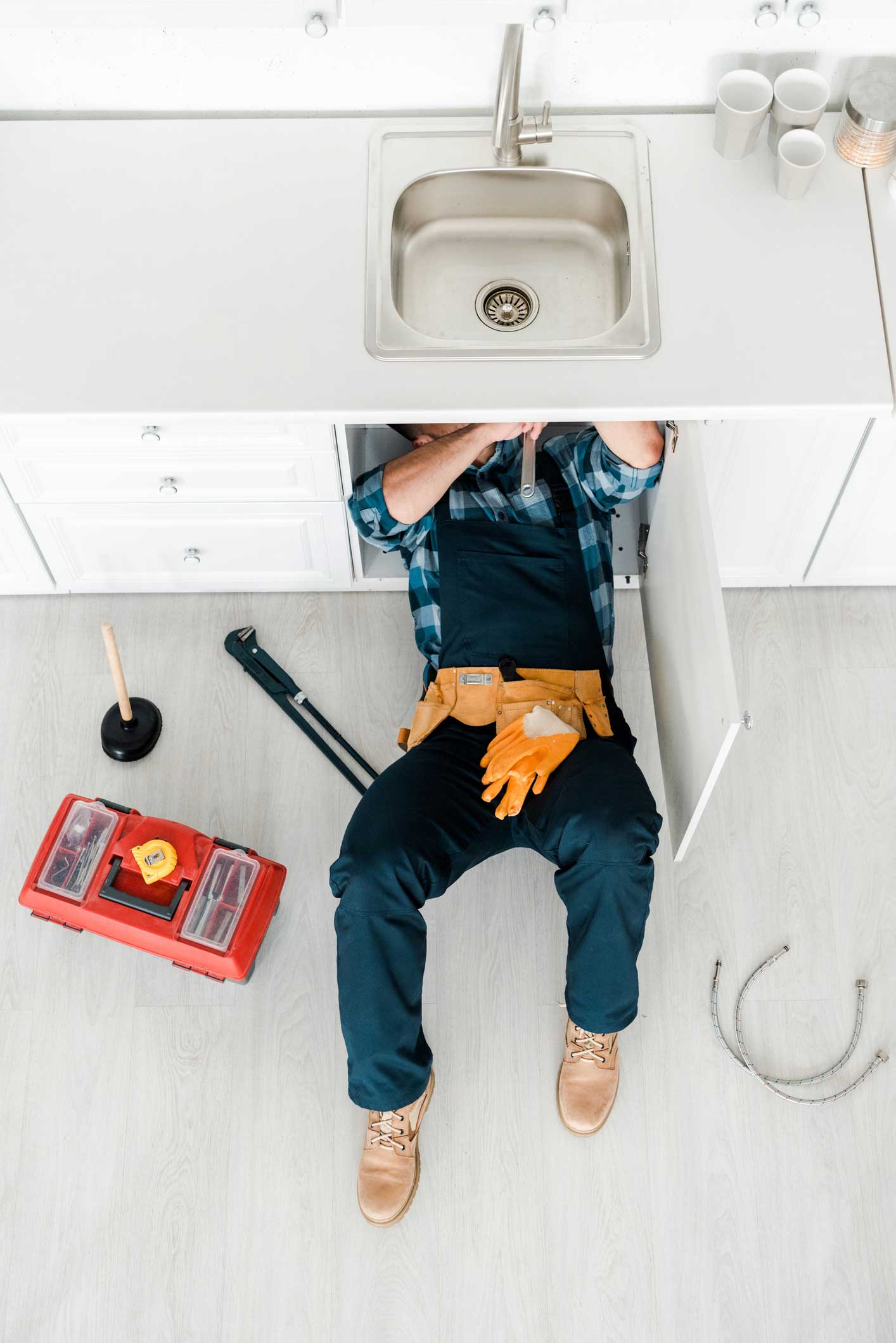 Plumber Lying On The Floor — Haslett, MI — Michigan Plumbing Plumber working under a kitchen sink, tools nearby.