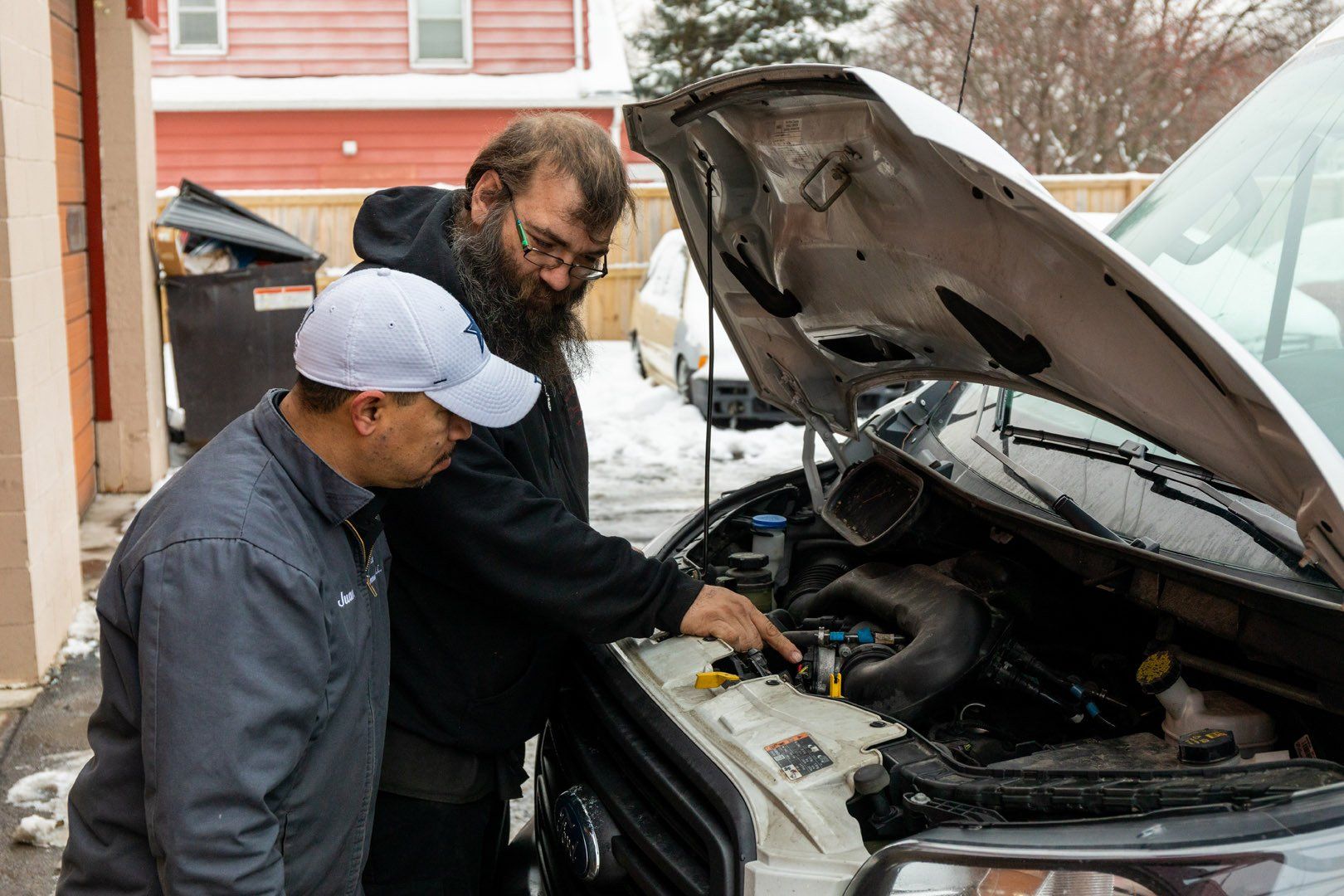 Two men examining a vehicle engine with the hood up. Snow present.