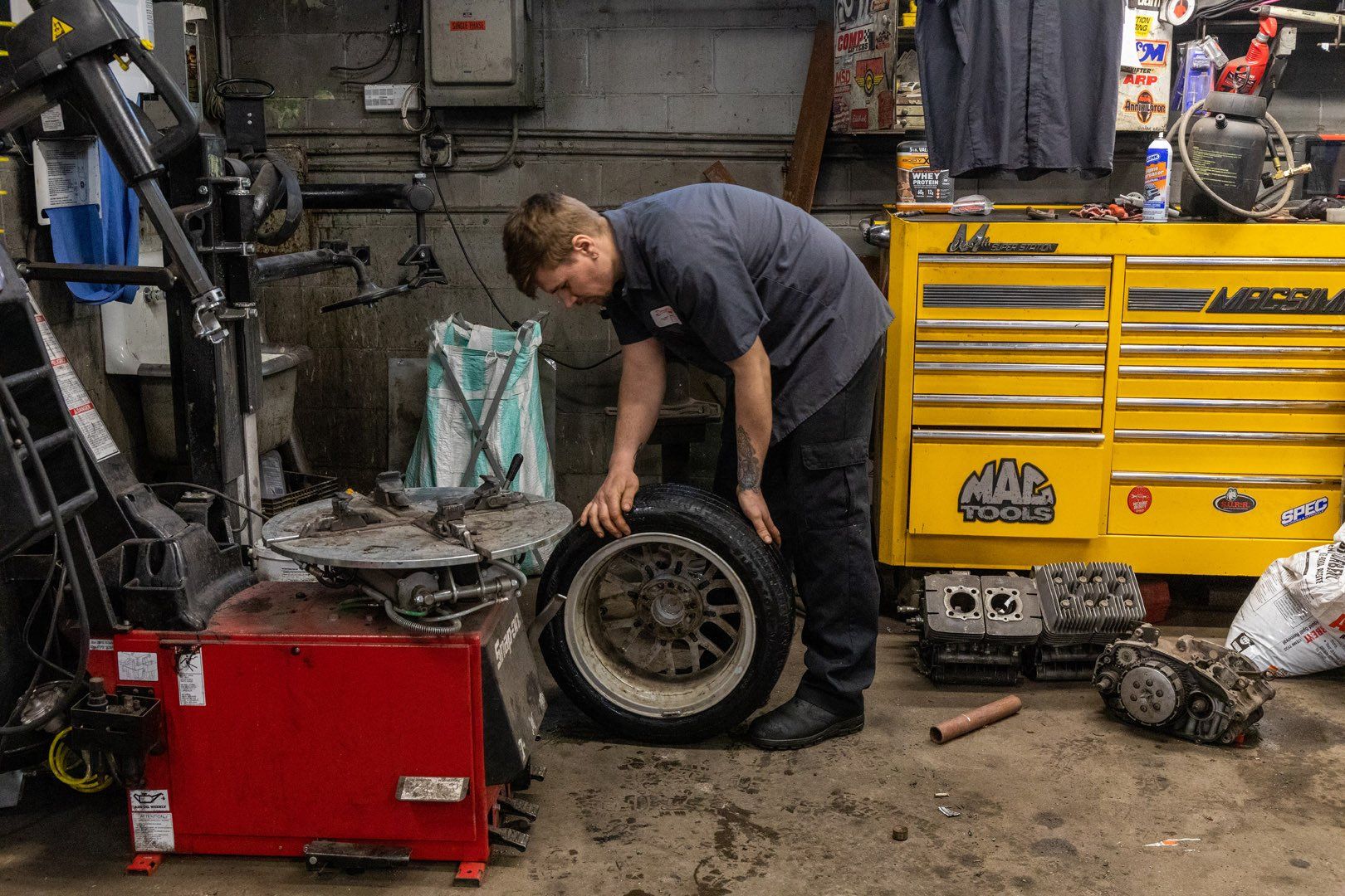 Mechanic in a garage with a tire, near tools and a yellow tool chest.
