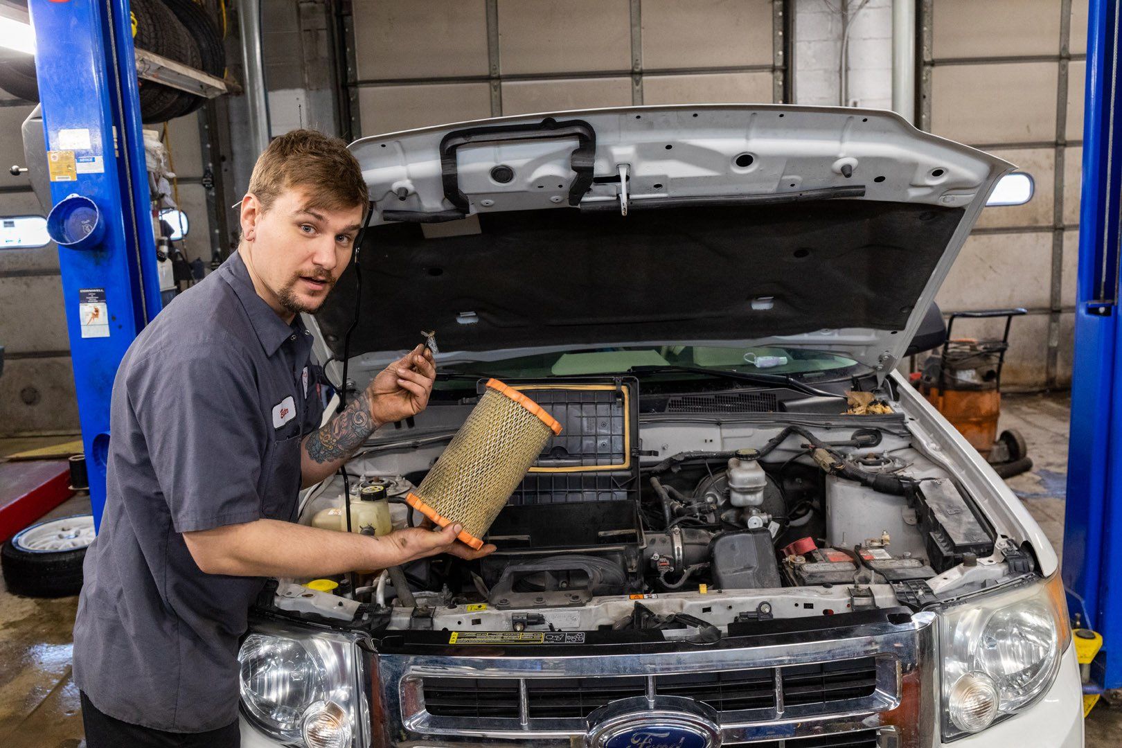 Mechanic holding dirty air filter in front of an open car hood in a garage.