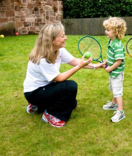 A woman is kneeling down next to a young boy holding a tennis racquet
