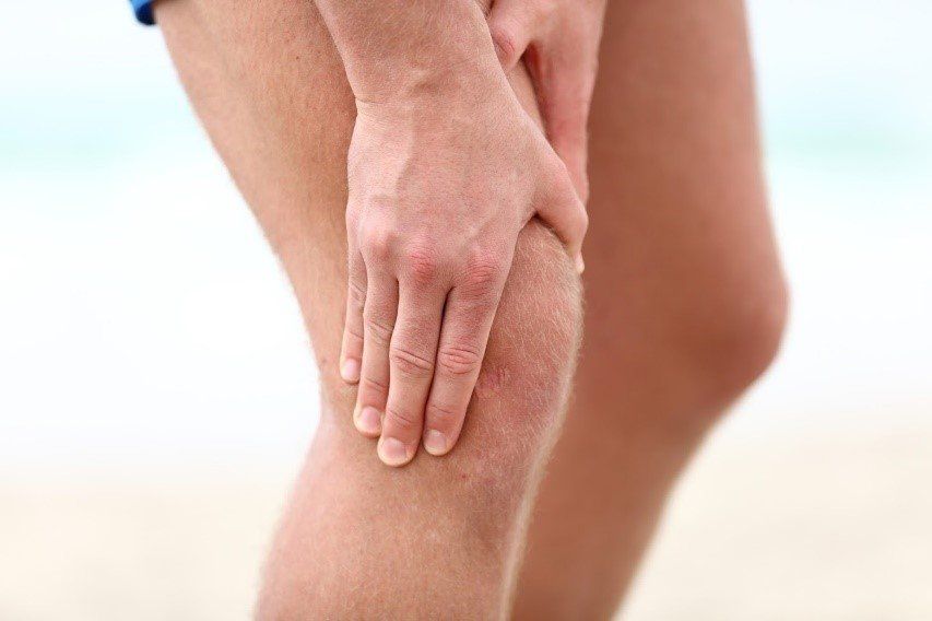 Person holding their hand over their knee, possibly experiencing pain; blurred beach background.