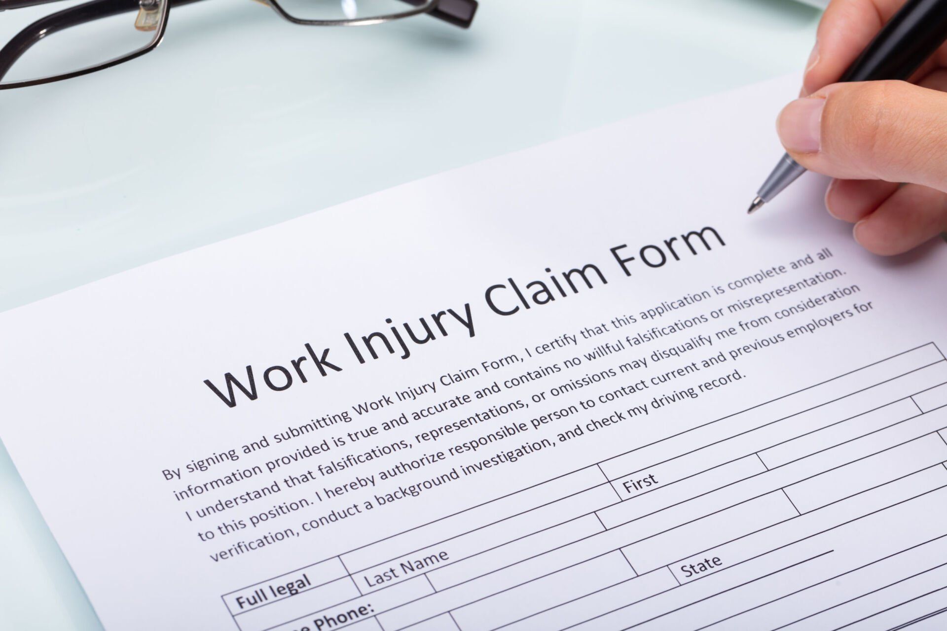 Hand filling out a work injury claim form with a pen on a desk