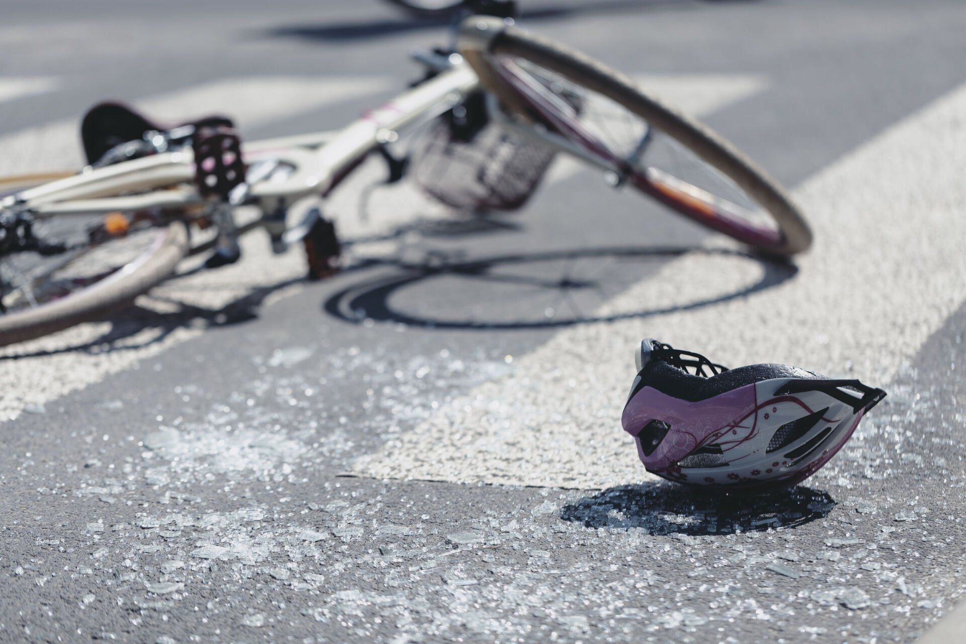 Damaged bicycle and broken helmet on sunlit road after crash