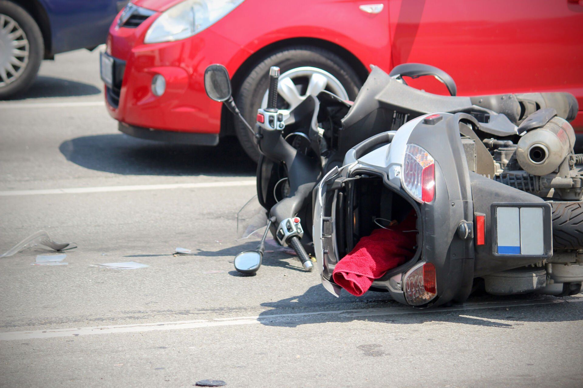 Overturned scooter in a street collision, with a red car and debris in the background.