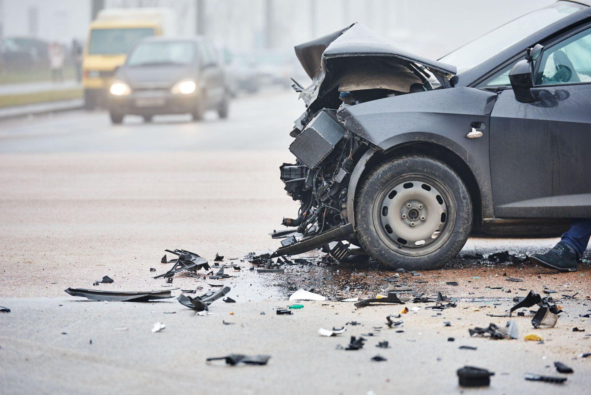 Damaged black car after a collision, with debris scattered on a wet road.