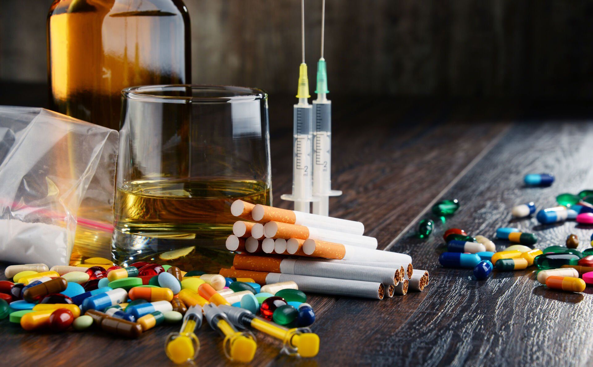 Scattered pills, syringes, and alcohol bottles on a table, suggesting substance abuse or overdose risk