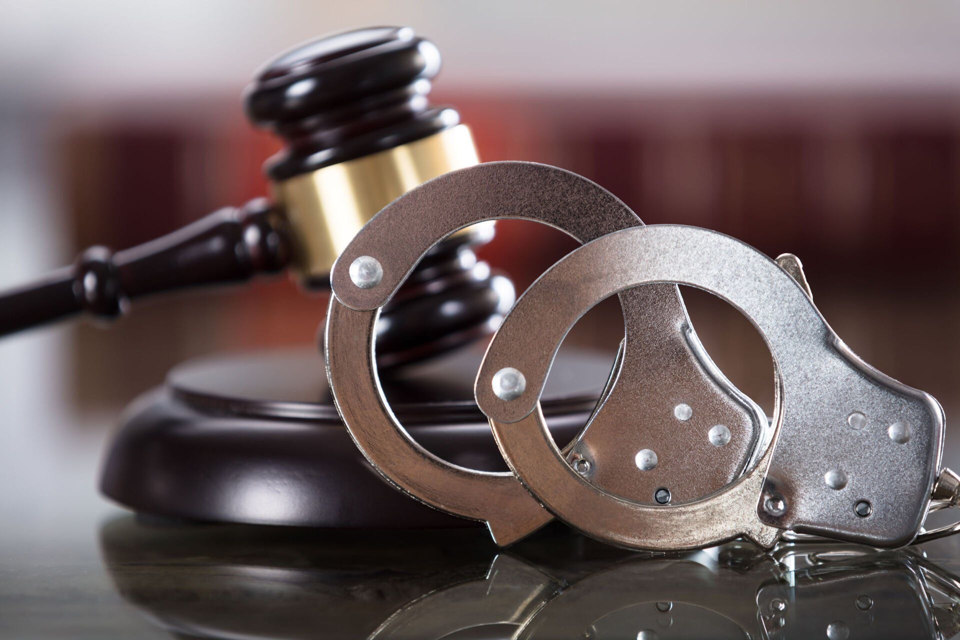 Handcuffs in front of a judge’s gavel on a reflective surface, symbolizing law and crime