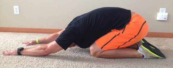 A man is kneeling on the floor stretching his legs.