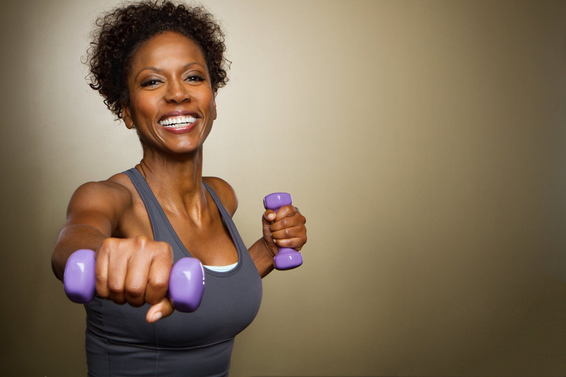 A woman is holding purple dumbbells in her hands and smiling.