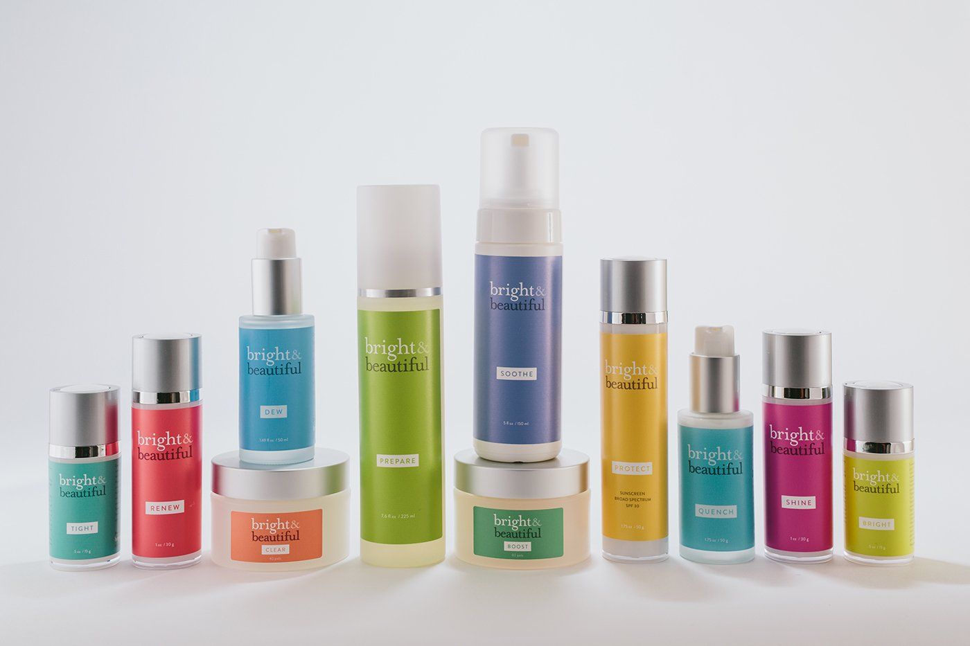 Assorted colorful cosmetic bottles and jars arranged in a row on a white background