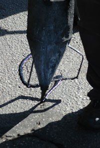 A worker pouring sealant onto asphalt with a pointed nozzle, surrounded by a metal frame.